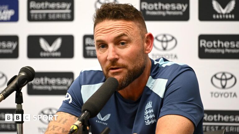 Brendon McCullum speaks into a microphone with sponsor's boards behind