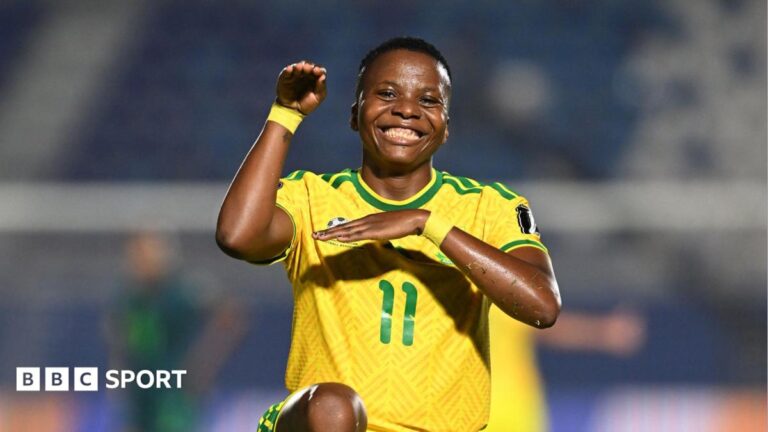 Thembi Kgatlana of South Africa smiles directly into the camera and strikes her trademark 'snake' celebration pose which sees her lift her right arm up with the hand tilted over as if to mimic a snake's head, with the left arm crossed horizontally across her chest and also with one knee raise off the floor up to waist level