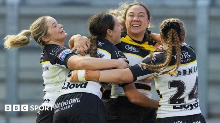 York Valkyrie forward Adaoha Akwiwu smiles broadly as she is mobbed by team-mates, all in white and back, after scoring a try against Leeds Rhinos.